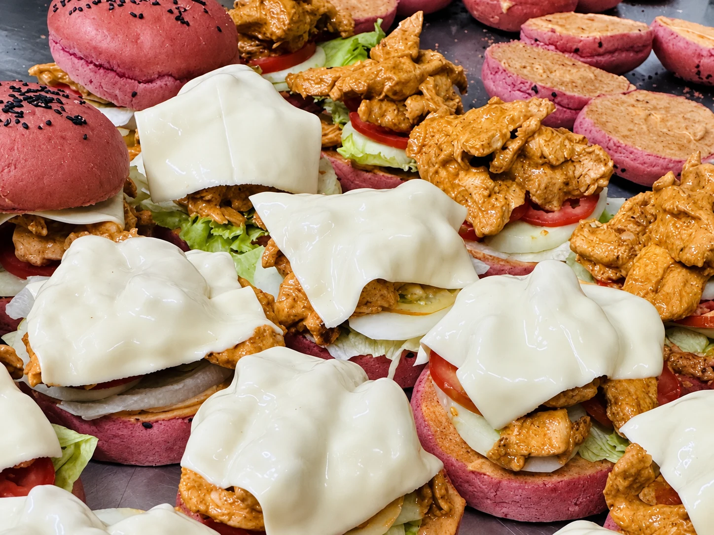 Pink beetroot burger buns with filling, vegetables and cheese during assembly in Carb Theory’s kitchen
