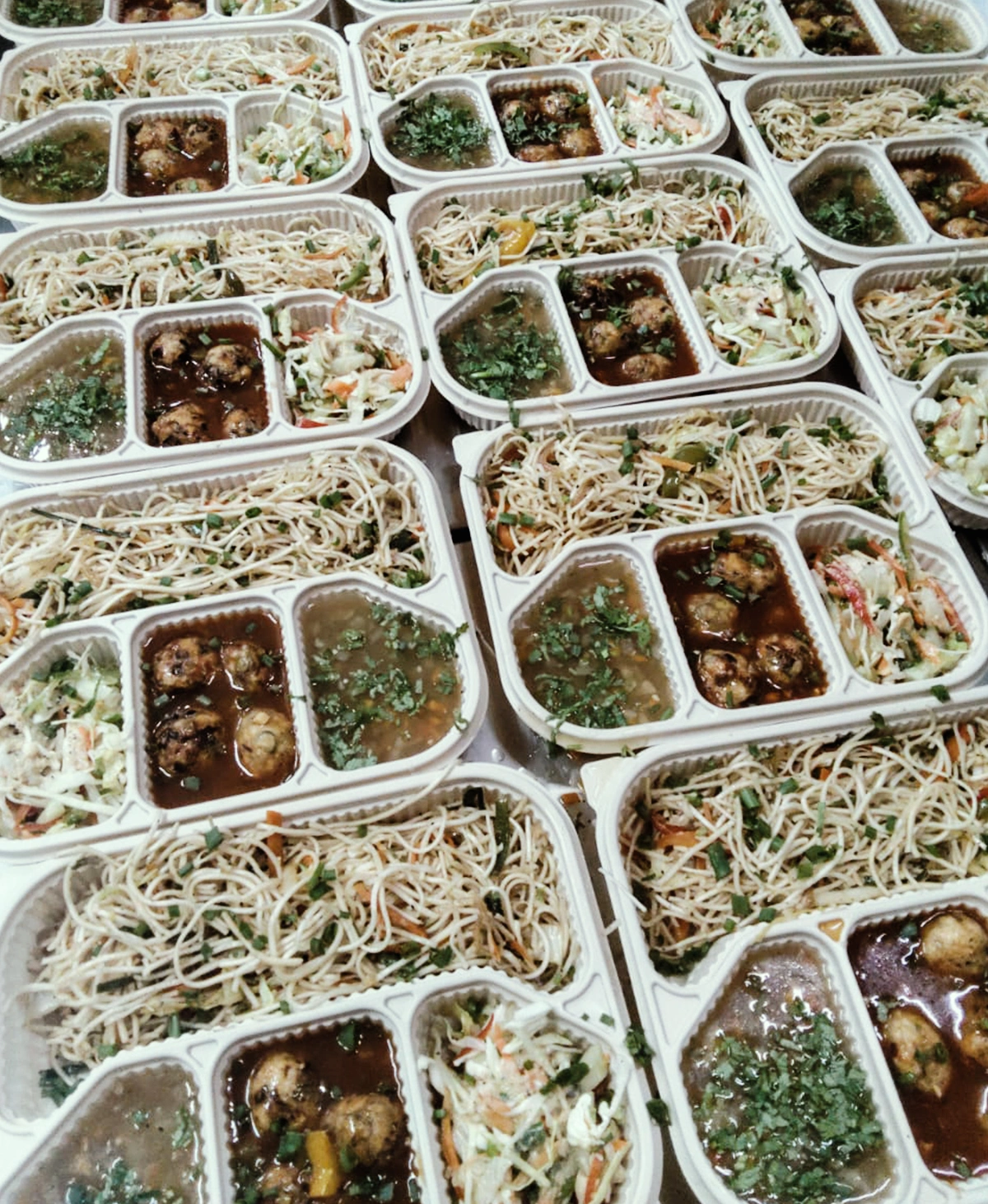 Compartmentalized boxes filled with noodles, gravy, and salad for corporate meals in Bengaluru