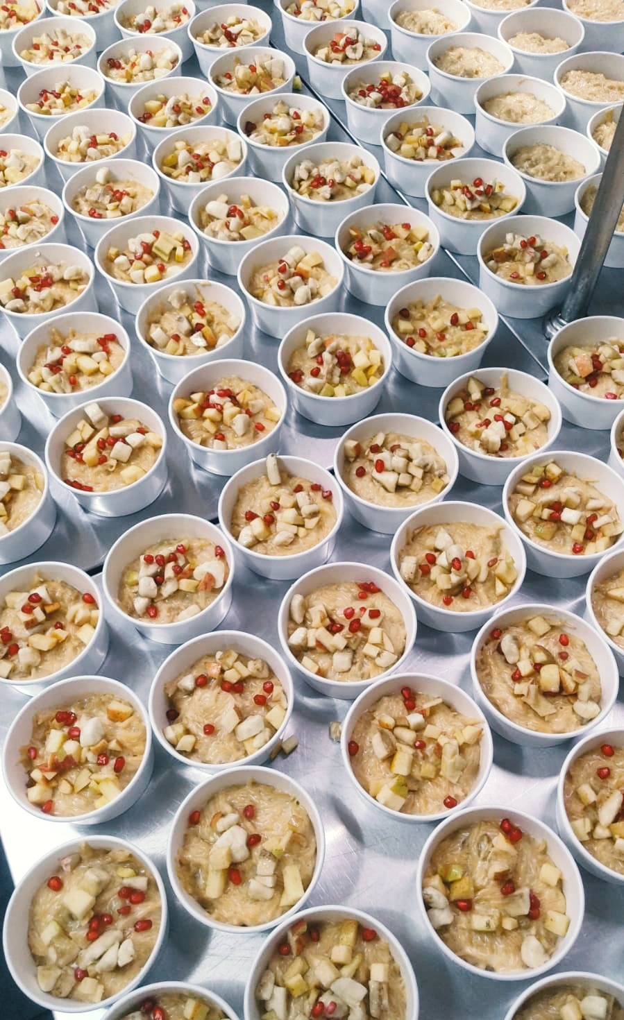Rows of individual fruit dessert cups topped with fresh fruits, pomegranate seeds and nuts, prepared for corporate catering